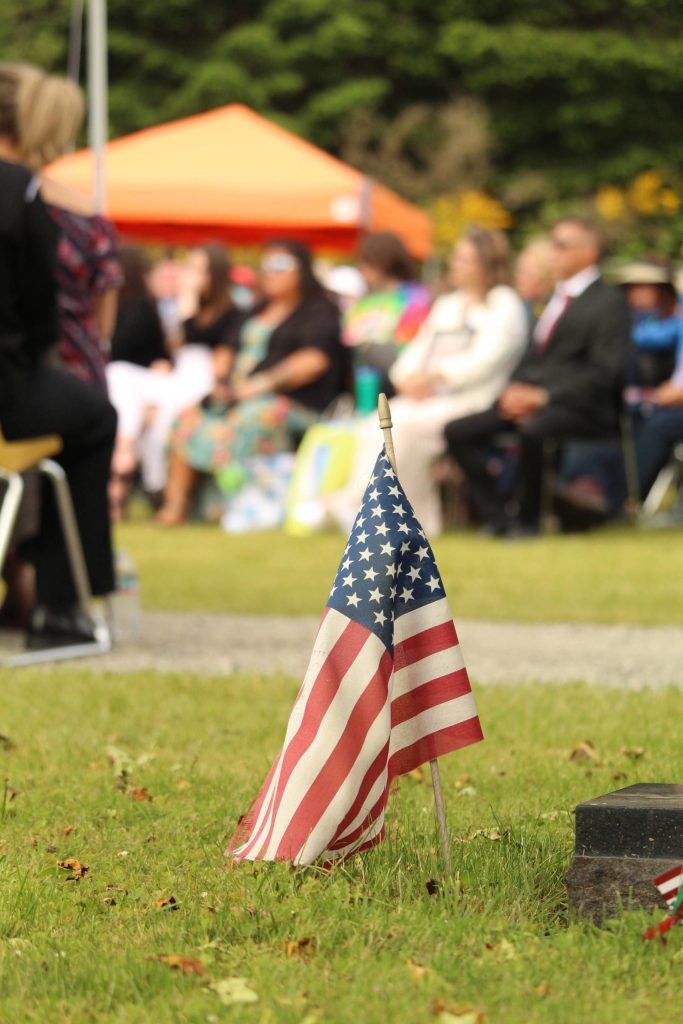 A flag marks a grave before the crowd.