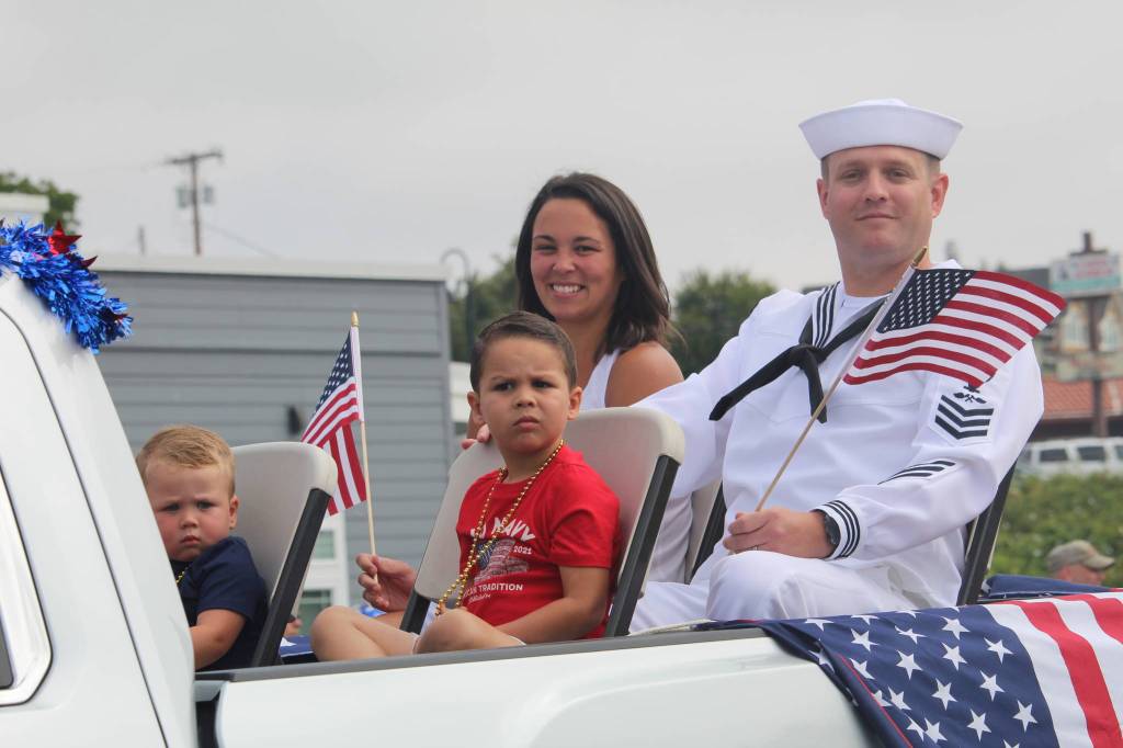 A sailor and his family wave American flags as they travel the parade route. (Photo by Karina Andrew/Whidbey News-Times)
