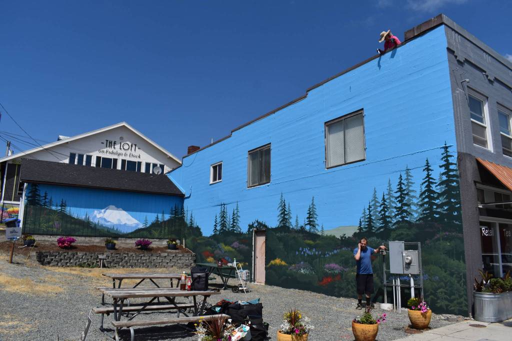 Photo by Emily Gilbert/Whidbey News-Times
Paula Fries working on a mural on the corner of Southeast Dock Street and Southeast Pioneer Way in downtown Oak Harbor. The mural spans two walls and features Mount Baker, rolling hills and a soon-to-be gate to a secret garden.