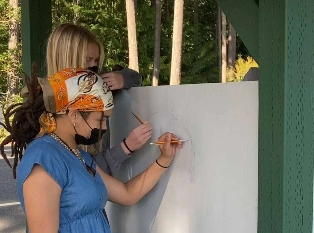 Junior Simone White, front, and senior Mikenna Wicher sketch on the side of the new farmstand. (Photo provided)