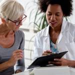 A female doctor sits at her desk and chats to an elderly female patient while looking at her  test results