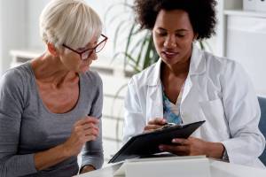A female doctor sits at her desk and chats to an elderly female patient while looking at her  test results