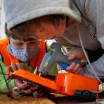 12-year old Caleb Arndt, left, holds part of a robot in place while Teddy Alexander, 12, solders. (Photo by David Welton)
