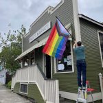 Business owner Cade Roach hangs a pride flag outside of Meet Market. (Photo provided)