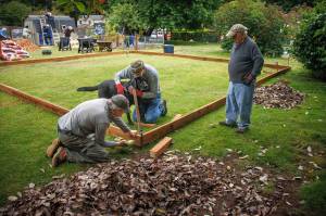From left to right, Jan-Marc Jouas, Russ DeWolfe and David LaBreque of Rotary Club of South Whidbey Island, with assistance from service dog Theo, work on building an enclosure for a playground in the backyard of the House of Hope.(Photo by David Welton)