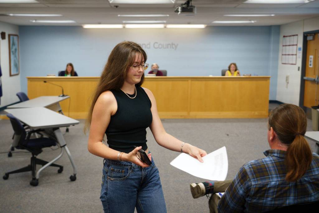 Photo by David Welton
Annie Philp distributes materials related to the United Student Leaders plea for county commissioners to adopt a climate emergency declaration during a meeting Tuesday.