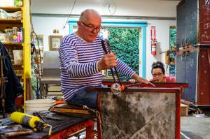 Photo by David Welton
John de Wit shapes a piece of glass while Catherine Marshall blows the glass.