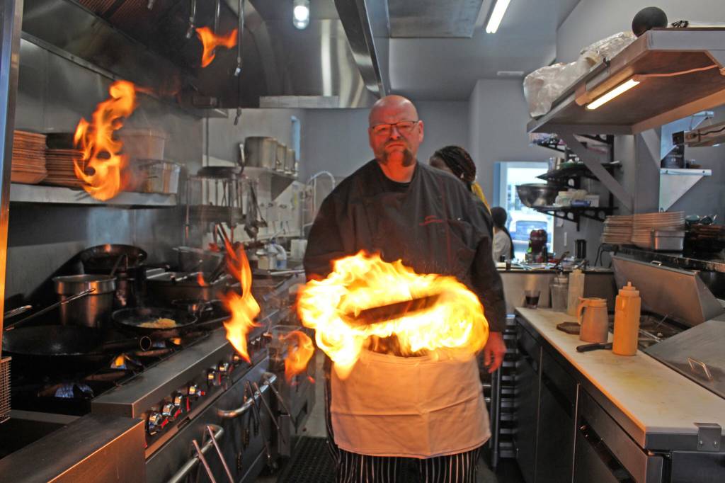 Chef Gordon Stewart adds a fiery flare to a dish in the kitchen at Gordons Fusion, a restaurant he opened this year. (Photo by Karina Andrew/Whidbey News-Times)