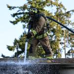 A North Whidbey Fire and Rescue firefighter works to extinguish a residential fire on Deer Park Lane May 25. (Photo by John Fisken)