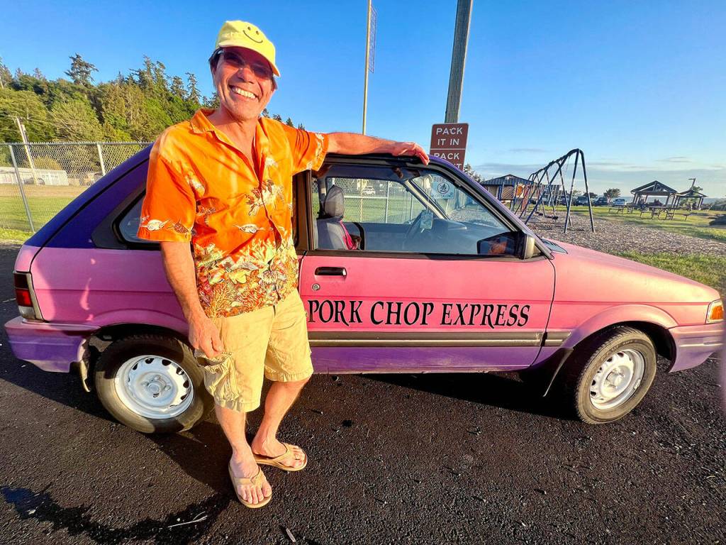 Dave Bronco Erickson stands next to the pink-and-purple 1991 Subaru Justy hatchback Pork Chop Express car that he is seeking to re-home for $500. The car nicknamed Porky has been on Whidbey Island for years, often as yard art. (Andrea Brown / The Herald)