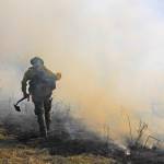A firefighter walks across the thick smoke holding a shovel. (Photo by Luisa Loi/Whidbey News-Times)