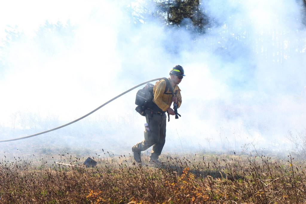 A firefighter drags a water hose to extinguish the flames. (Photo by Luisa Loi/Whidbey News-Times)