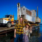 Photo by David Welton
Tevon Dubois and Chanel Jost pose in front of their house as it is loaded onto a truck at a Possession Point dock.