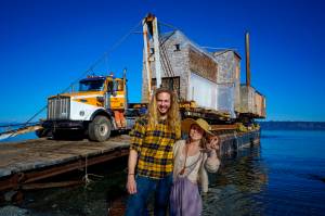 Photo by David Welton
Tevon Dubois and Chanel Jost pose in front of their house as it is loaded onto a truck at a Possession Point dock.