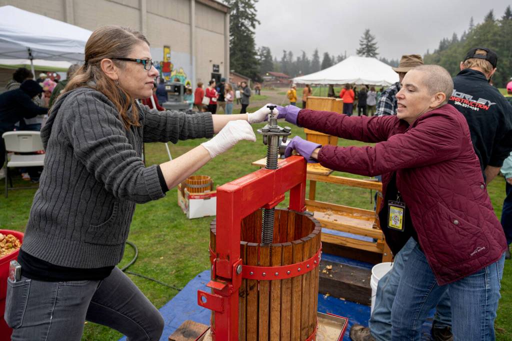 Woodhaven High School co-administrators Heidi Nelson and Marli Jenkins, right, work the apple press together. (Photo by David Welton)
