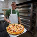 Paul proudly presents a finished pizza. He and his wife, Lila, recently started a take-and-bake pizza business. (Photo by David Welton)