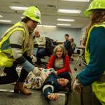 Public Health Office Manager Melissa Overbury-Howland (left), Commissioner Melanie Bacon (back) and Board Clerk Jennifer Roll (right) tend to Chris Brooks during an earthquake demonstration at the commissioners meeting on Wednesday. (Photo by Sam Fletcher)