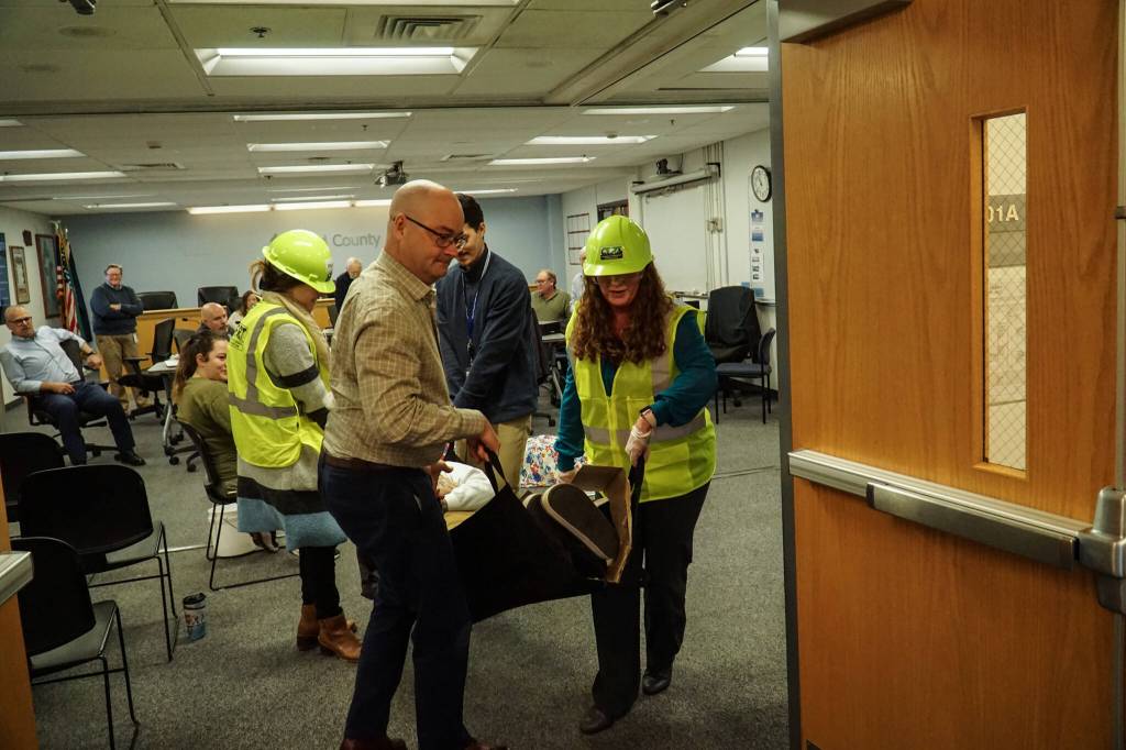 Island County Planning Manager Michael Jones, at left, Health Director Shawn Morris (back) and Board Clerk Jennifer Roll, at right, carry an actor during an earthquake demonstration at the commissioners meeting on Wednesday. (Photo by Sam Fletcher)