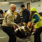 Island County Planning Manager Michael Jones (left), Health Director Shawn Morris (back) and Board Clerk Jennifer Roll (right) carry an actor during an earthquake demonstration at the commissioner's meeting on Wednesday. (Photo by Sam Fletcher)