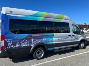 The two newest members of the fleet are the E Ford 350EL model Lightning eMotors battery electric vehicles donning the organization’s brand-new design: stripes of green, blue and purple gradients behind simple linework of orcas, homes, trees and sunshine. (Photo courtesy of Island Transit)