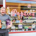 Andy Plumlee stands in front of Popsies, a sweet treats store in downtown Oak Harbor, while holding bags of flavored popcorn.