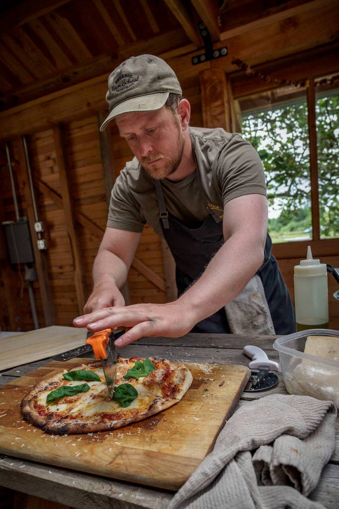 Adam Skaardal, hospitality and business manager for the Organic Farm School, slices a wood-fired pizza. (Photo by David Welton)