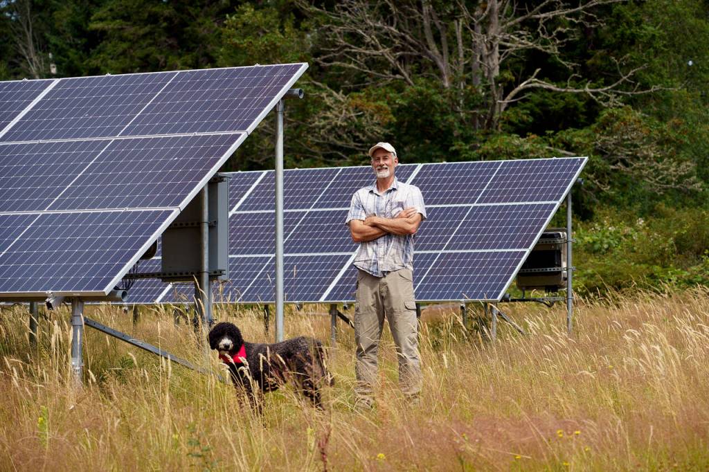 (Photo by David Welton)
Britt Fletcher and Shep the farm dog stand before an array of solar panels. Earlier this year, Mutiny Bay Blues was awarded a $78,800 grant from USDA to purchase and install them.