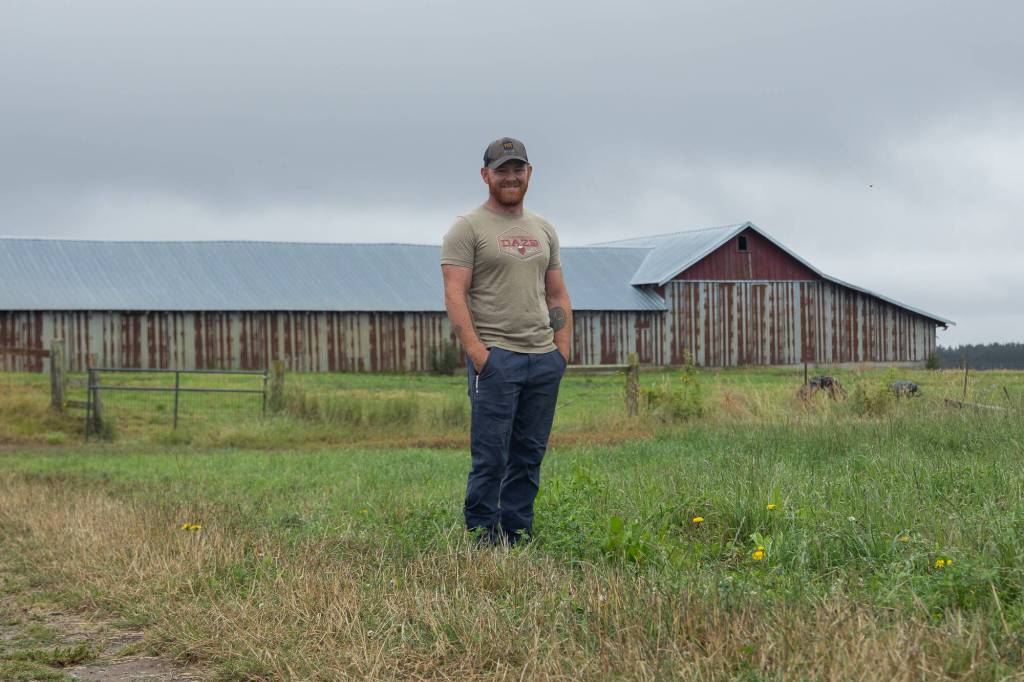 Farmer Kyle Flack poses for a picture in front of the his barn on Bells Farm, July 30. (Photo by Caitlyn Anderson)