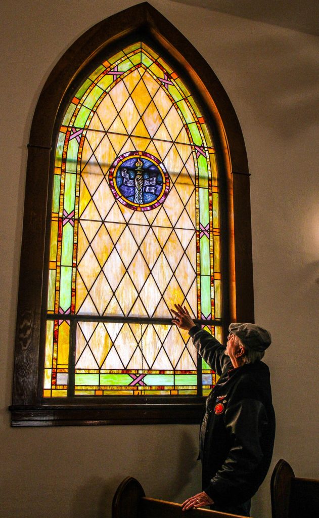 (Photo by Luisa Loi)
Bill Waite admires one of 13 stained glass windows in the church. The art depicts a hand holding a torch and the words The Lord is My Light.