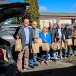 (Photo by Luisa Loi)
At left, Reid Schwartz, Jim Slowik, Lyn Bartley, Ken Hulett, Tony Bartley, Dave Williams and Christy Schwartz form a chain to place bags of food inside a car before theyre delivered to schools.