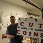 (Photo by Kira Erickson/South Whidbey Record)
South Whidbey artist Chris Soukup holds up a sign in his studio informing people that his coin pendants are cut by hand, without the use of machines or lasers.