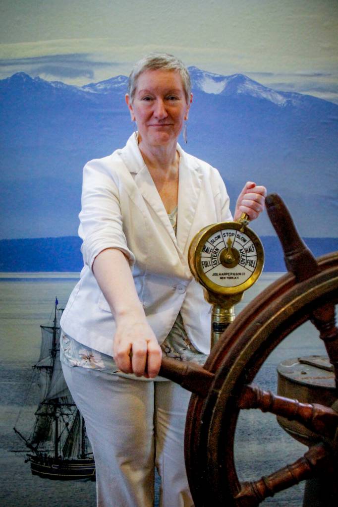 Dalva Church, executive director for Island County Historical Society, gets behind a ships wheel in the new maritime exhibit at the Coupeville museum. (Photo by David Welton)