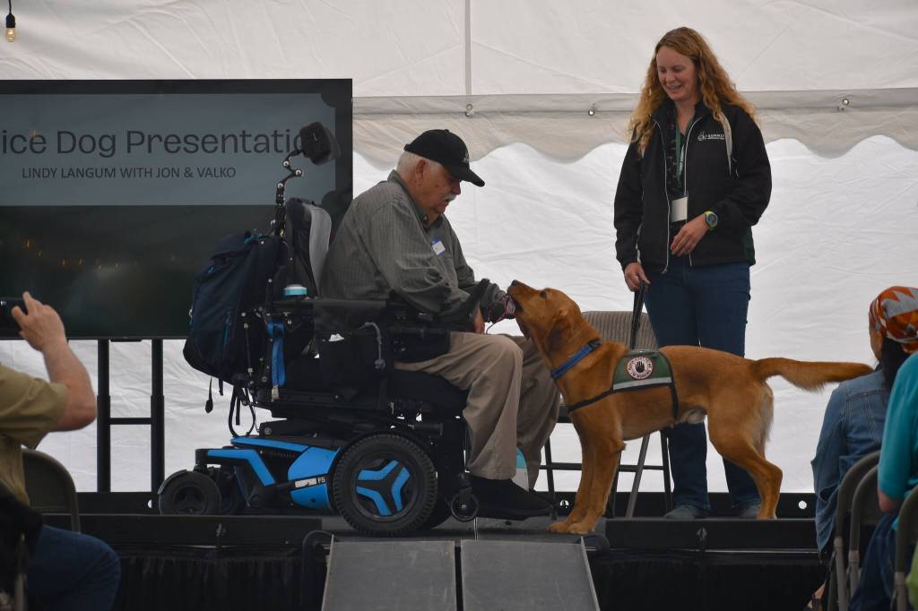 (Photo by Emily Gilbert) Jon Palmason and dog Valko demonstrate how the canine can help with daily tasks  such as picking up dropped reading glasses  to help him live more independently. Summit Assistance Dogs staff trainer, Lindy Langum, right, worked with the pair to train Valko to be an assistance dog.