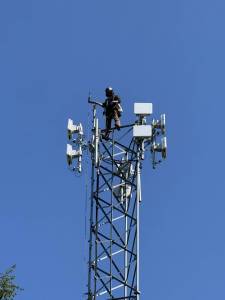 Astound technician installing fixed wireless network transmission devices atop existing headend tower.