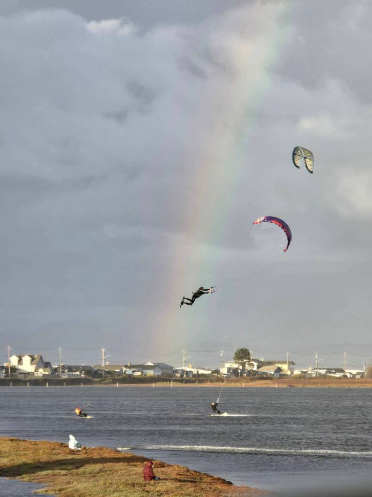 (Photo by Nichol Redfearin)	A kiteboarder launches into the air superman-style, with onlookers watching in awe.