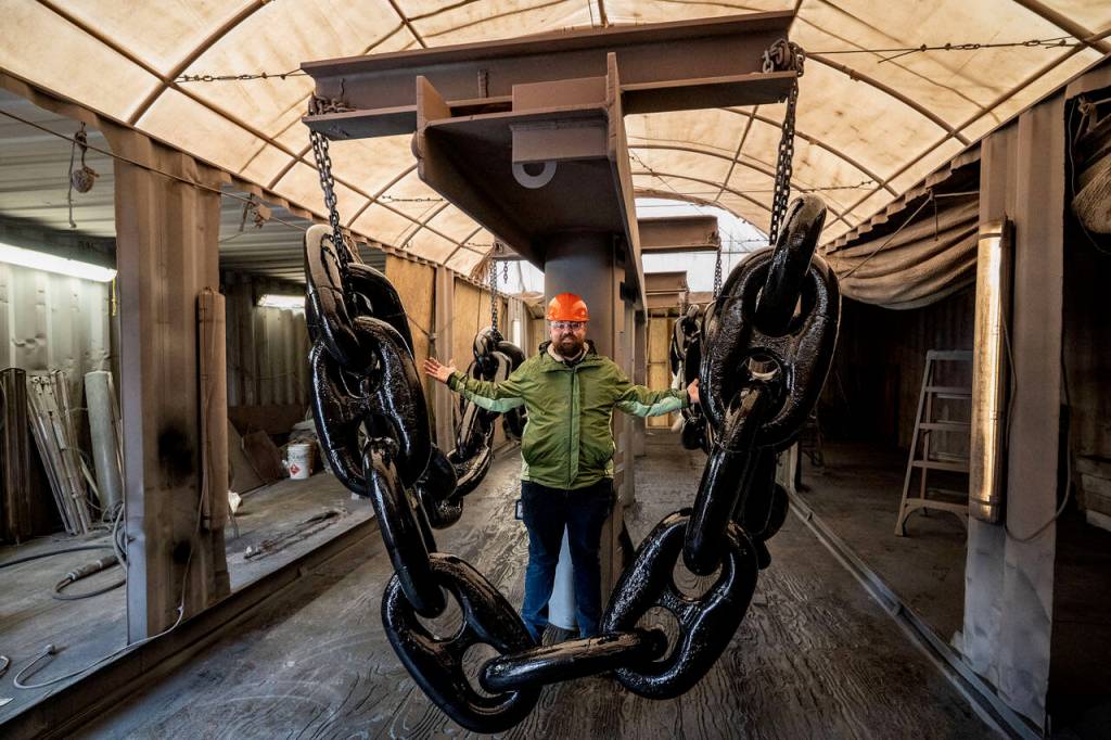 (Photos by David Welton) Senior Recruiter Dane Douglas stands behind a chain of giant, freshly painted links used to anchor massive vessels. Each link weighs a few hundred pounds.