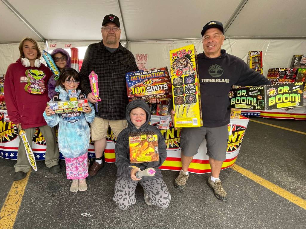 (Photo by Marina Blatt) The Church of the Nazarene fireworks stand is open daily from about 10 a.m. to 10 p.m. through the Fourth of July near the Sherwin-Williams Paint Store in Oak Harbor. Volunteers and their kids hold up a variety of items they sell, from the 100-shot Declaration of Detonation to the Mighty Sword.
